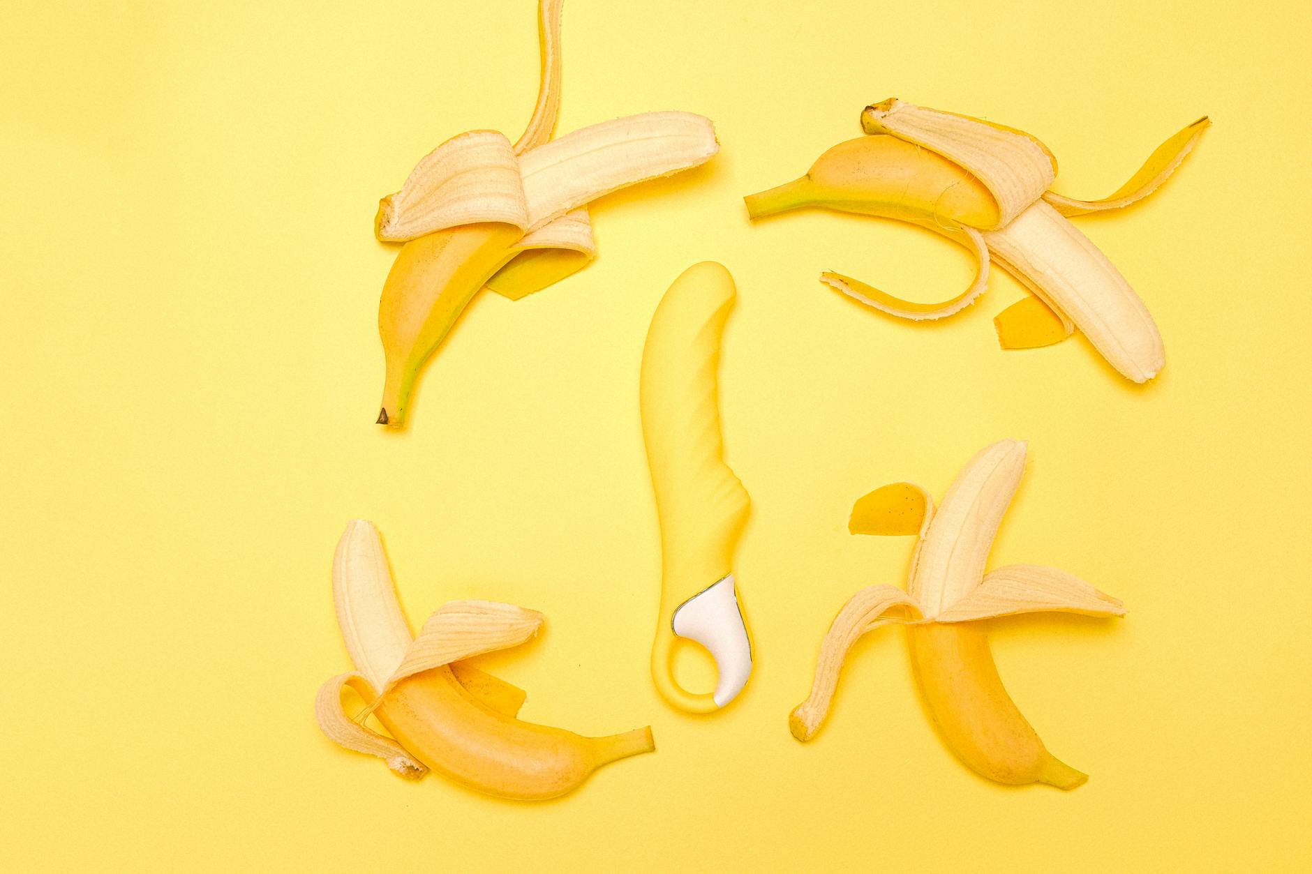 Yellow silicone lemon vibrator surrounded by fresh citrus on a bright yellow background