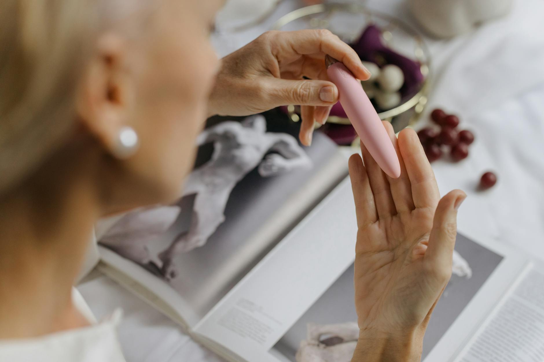 Woman holding a vibrator with art books in background, representing intimate self-care during time apart
