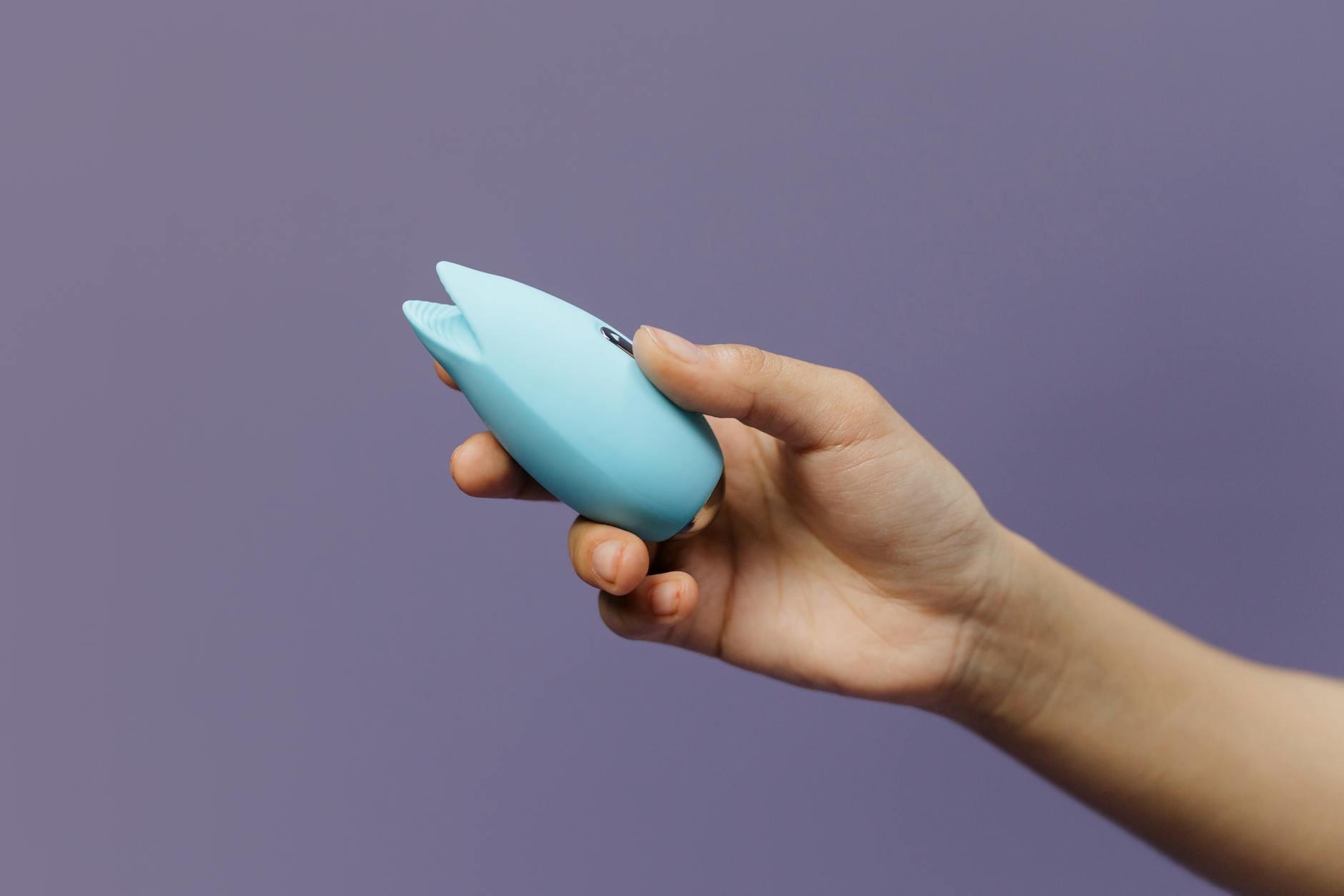 A blue silicone clitoral vibrator held in hand, representing sexual wellness and self-pleasure