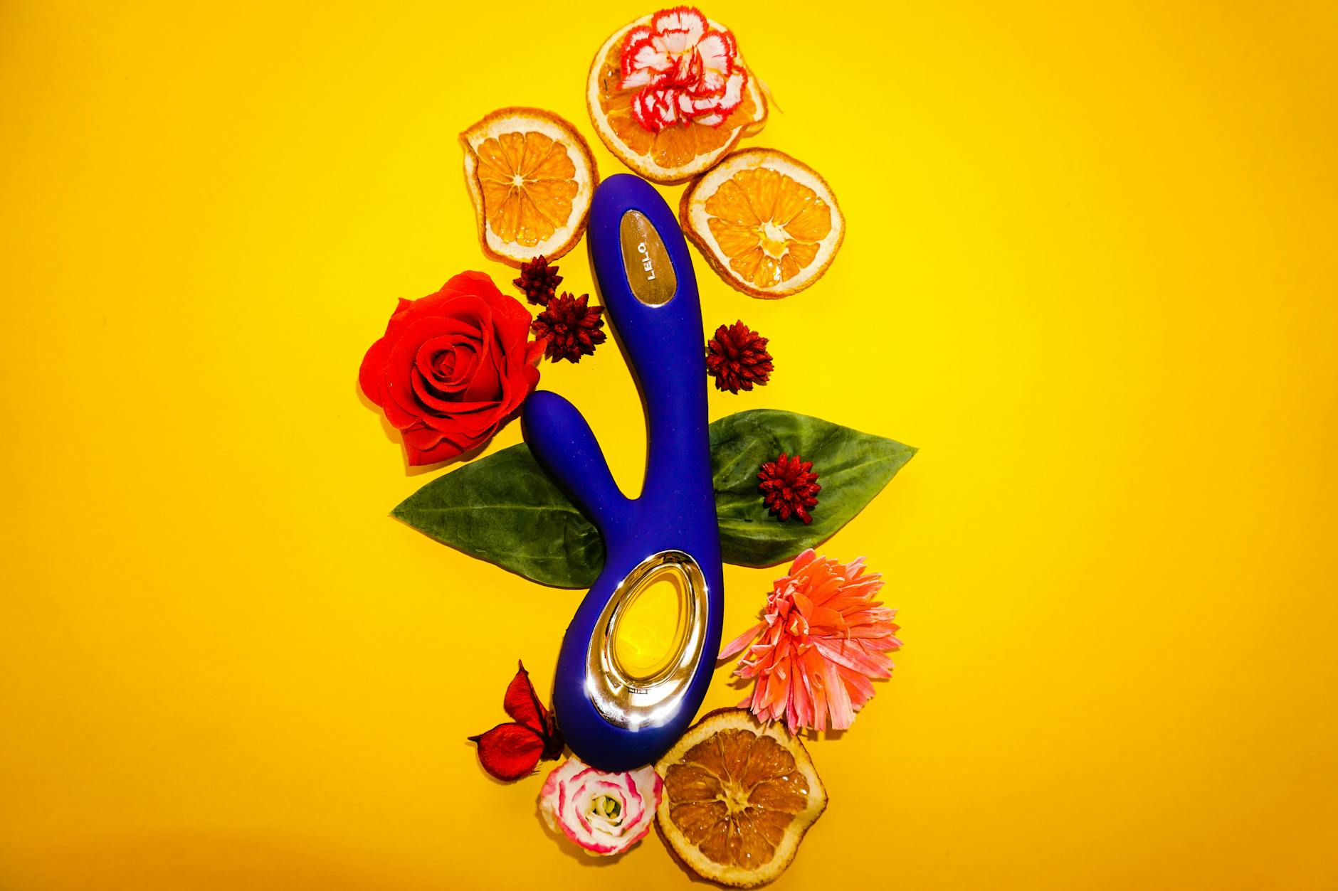 Vibratore blu Lemon Sucker circondato da fiori e fette d'arancia su sfondo giallo
